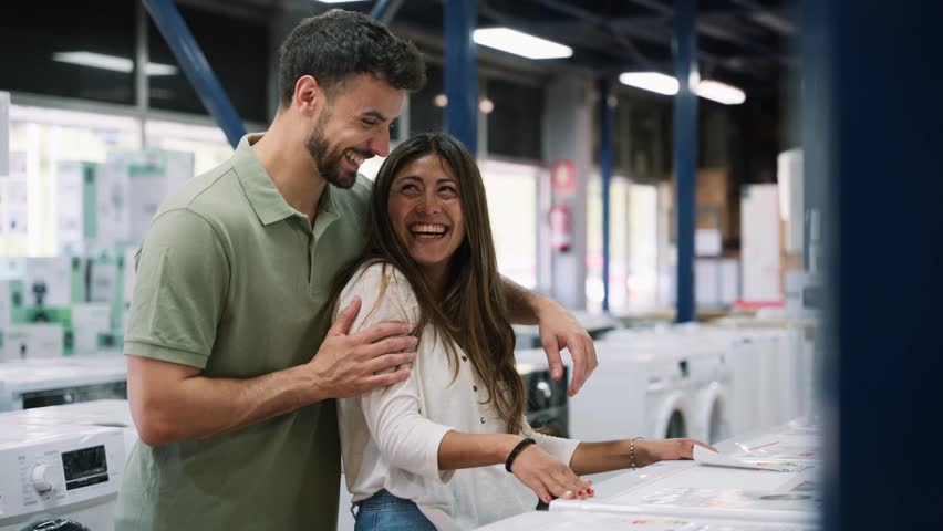 Joyful couple shopping together in a home appliance store. The man and woman are laughing and talking while choosing a new washing machine