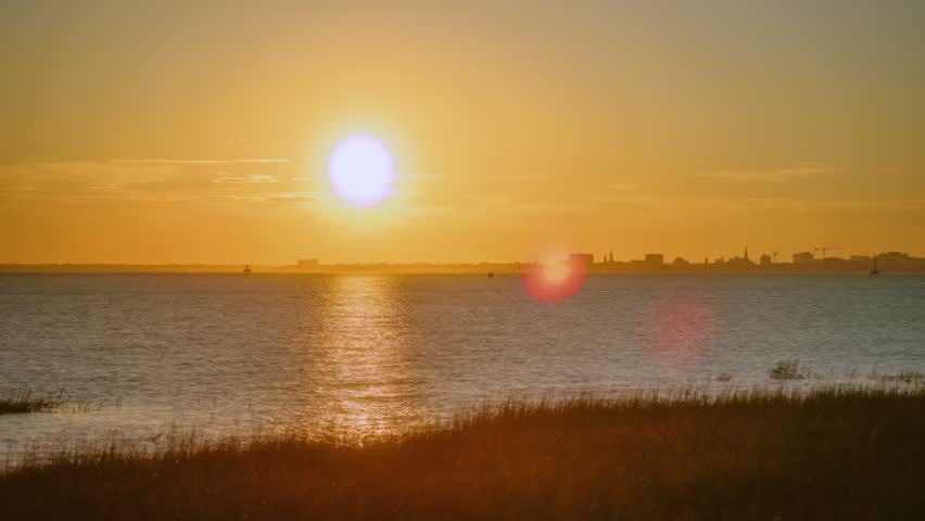 Warm spring timelapse of a bright orange sunset over the coastal city of Charleston, SC. Shot at the Pitt Street Bridge as waves roll into the harbor and boats whir by.