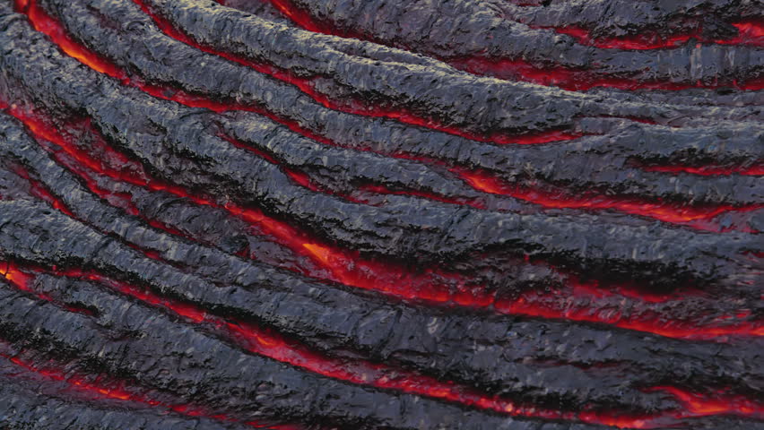 Extreme close-up of glowing magma visible through cracks in a cooling lava crust at Kīlauea Volcano, Hawaii. Flowing lava creates striking textures and patterns.