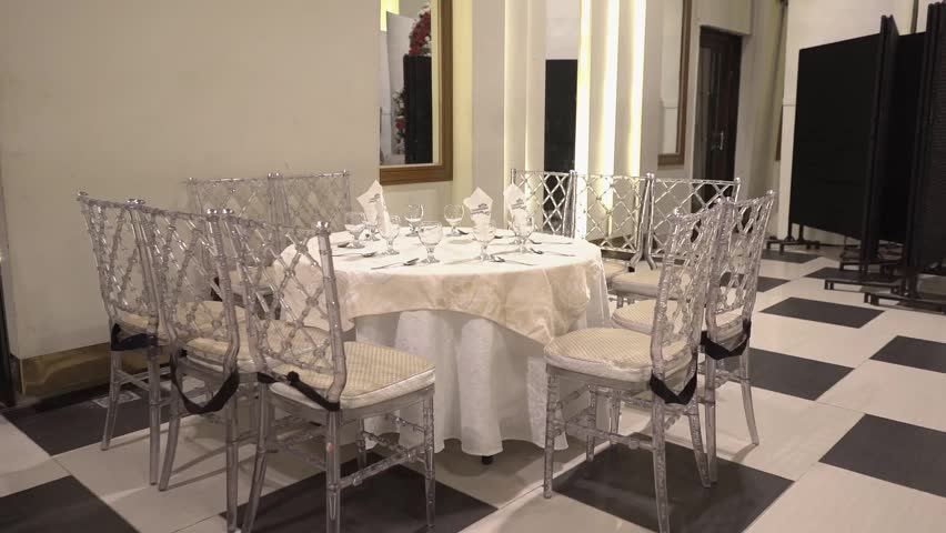 Elegant wedding banquet table setup featuring luxury transparent chairs, white table linens, and sophisticated reception décor inside a modern event hall. Stylish dining arrangement with soft ambient lighting, perfect for wedding receptions, formal events, celebrations, hospitality, and luxury interior decoration concepts.