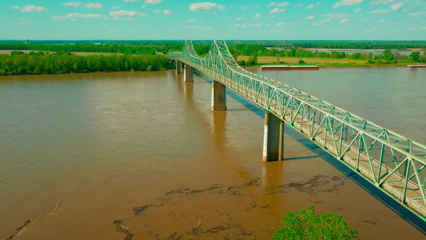 Green steel cantilever bridge spanning the muddy Mississippi River, illustrating aging American infrastructure, interstate freight logistics, and civil engineering.