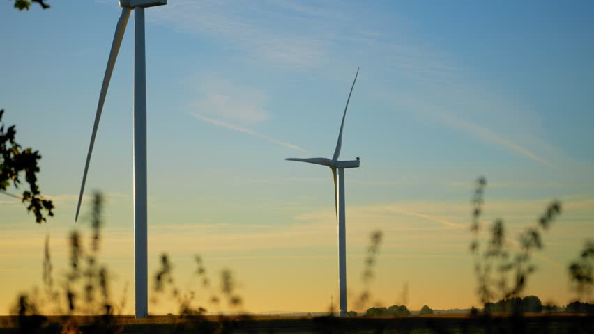 Large modern wind power generators silhouetted against an orange sky
