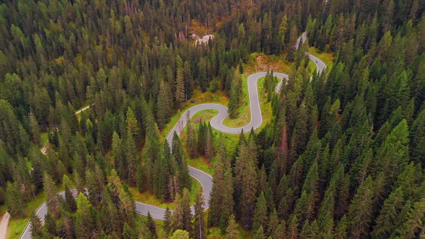 Iconic winding mountain road leading to Passo di Giau in the Italian Dolomites. Aerial view of a serpentine pass surrounded by a dense fir tree forest on a cloudy autumn day.