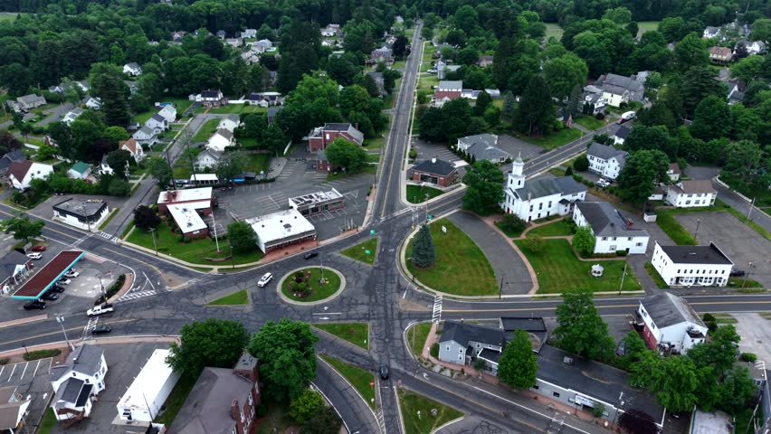 Drone pullback over the roundabout intersection near East Longmeadow Town Hall and white church, revealing a lush green suburban town with residential streets in Massachusetts.