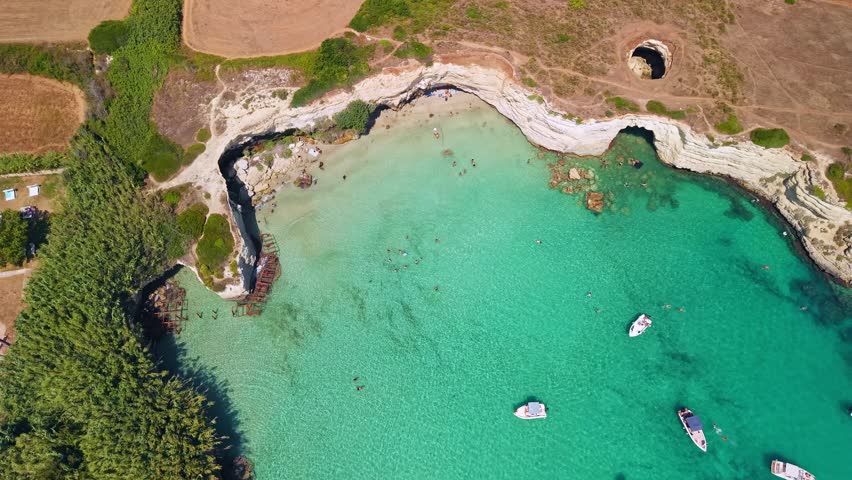 Aerial view of Grotta Sfondata sea cave on the Salento coast. The broken limestone roof reveals a turquoise lagoon with crystal clear water near Otranto during a sunny summer in Italy.