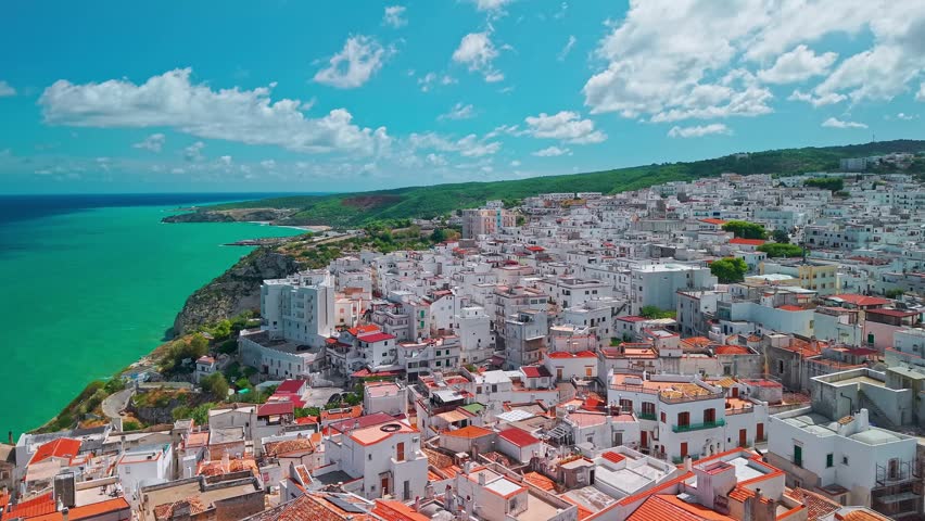 Aerial view of Peschici resort town on a sunny day in Puglia, Italy, popular Mediterranean destination with historic architecture, coastal cliffs, sandy beaches, and clear blue sea.