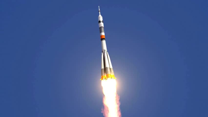 Russian Soyuz rocket ascending into a clear blue sky with blazing bright engine fire
