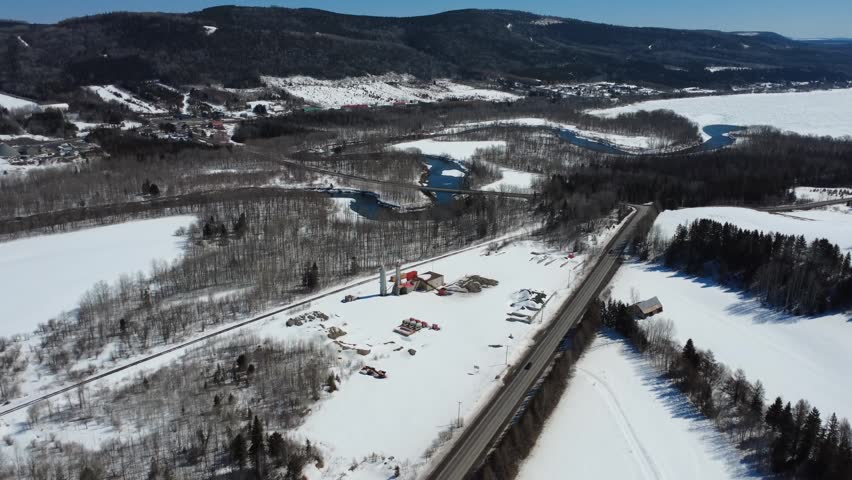 Expansive winter landscape featuring the Matapedia River, a road bridge, snow-covered forests, and the foothills of the Appalachian range.