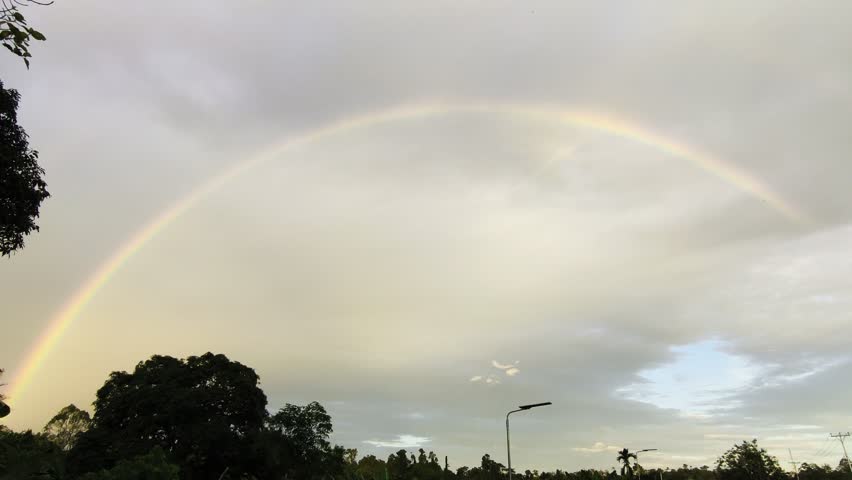 An amazing double rainbow arches over the rural landscape. The rainbow arches across the evening sky. 