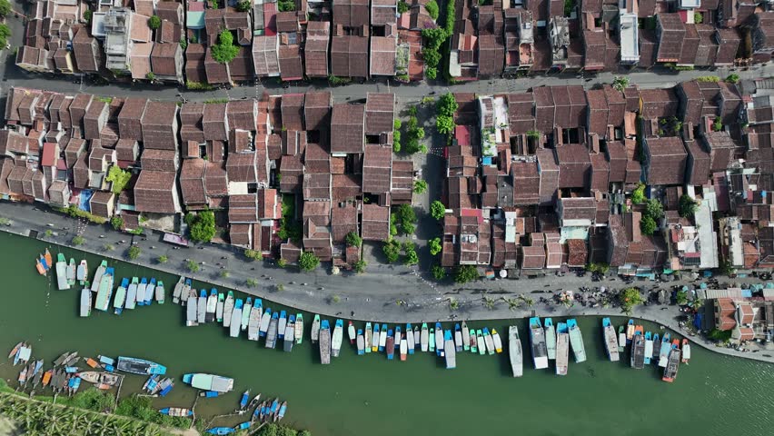 Boats moored along the riverbank beside historic neighborhoods in Hoi An viewed from above.
