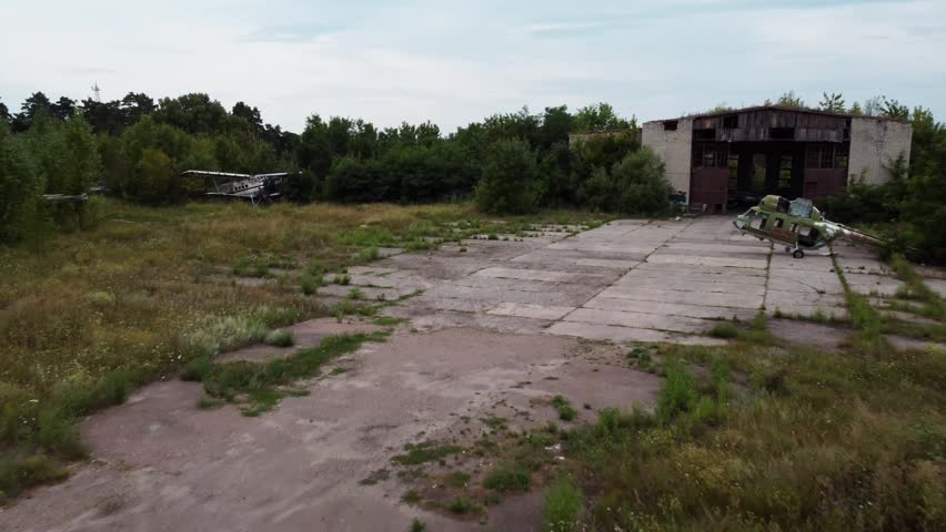 Aerial view of abandoned airbase with retired airplanes, old helicopter on concrete and weathered hangar in greenery