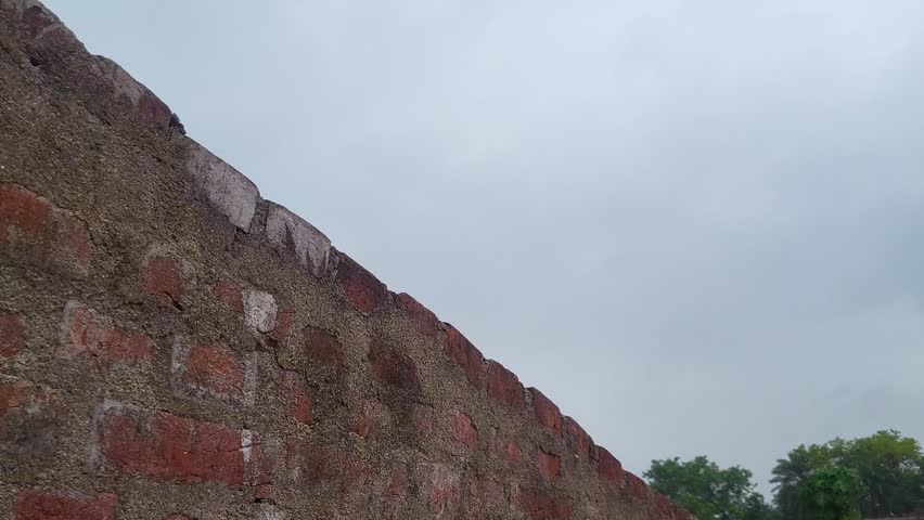 Red brick wall surface against overcast weather with birds flying across cloudy sky view.