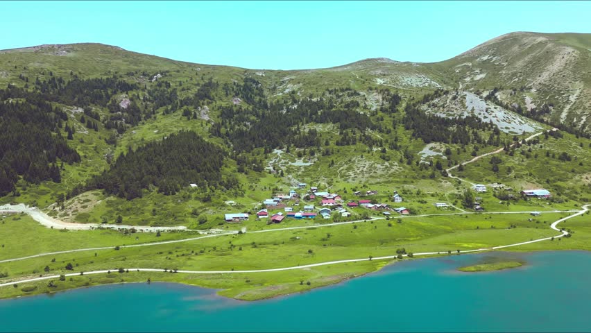 In the foreground, a deep blue pond; behind, mountain houses; and in the very background, the treeless peak of Ilgaz Mountain.