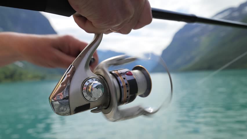 Close up view of fishing reel spinning with green lake water in motion.