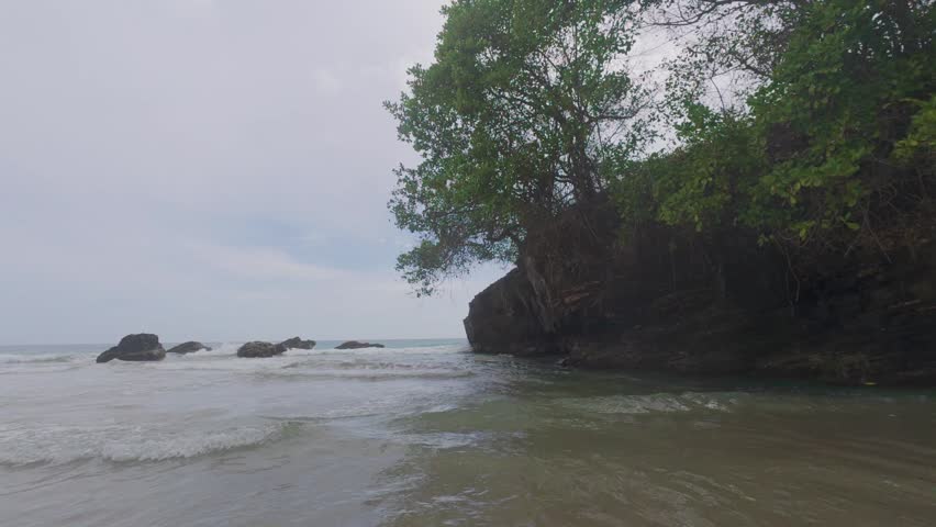 Spectacular panoramic view of a wild and secluded idyllic cove, with ocean waves crashing against the shore on a cloudy day