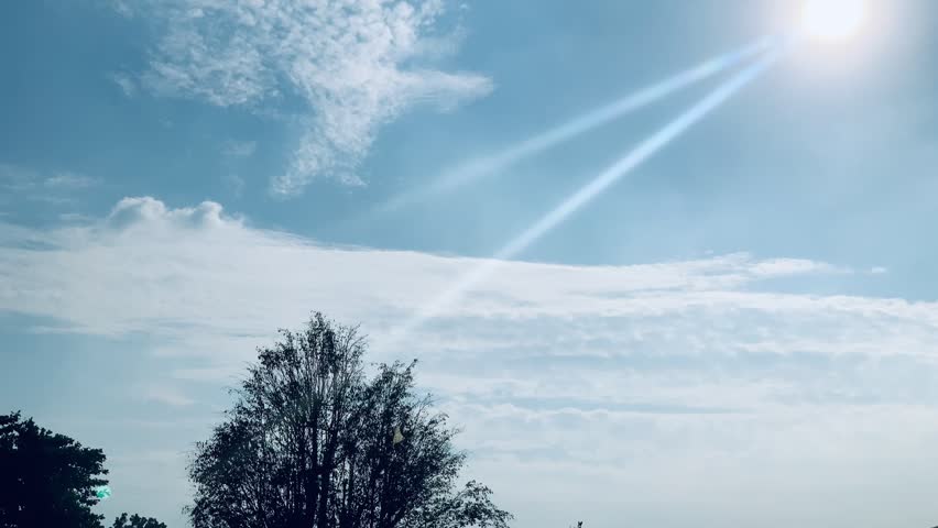 4K wide-angle sky over Jakarta, Indonesia, with complete sun and radiant lens flare above tree silhouettes. Crisp clouds, vivid blue tones and peaceful daylight mood, ideal for nature, weather and background themes.