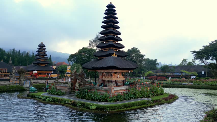 Aerial view of iconic Ulun Danu Beratan Temple surrounded by water and gardens on Lake Beratan, Bali. Traditional Balinese architecture in a peaceful mountain setting.