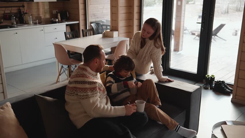 Son sits on the couch and eats from a cup while talking to his father and mother who are sitting next to him