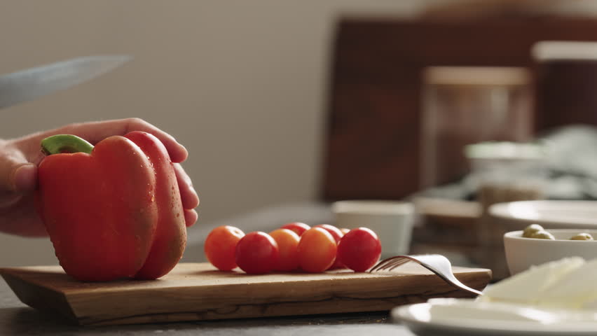 Close-up of red bell pepper being sliced on wooden cutting board with cherry tomatoes