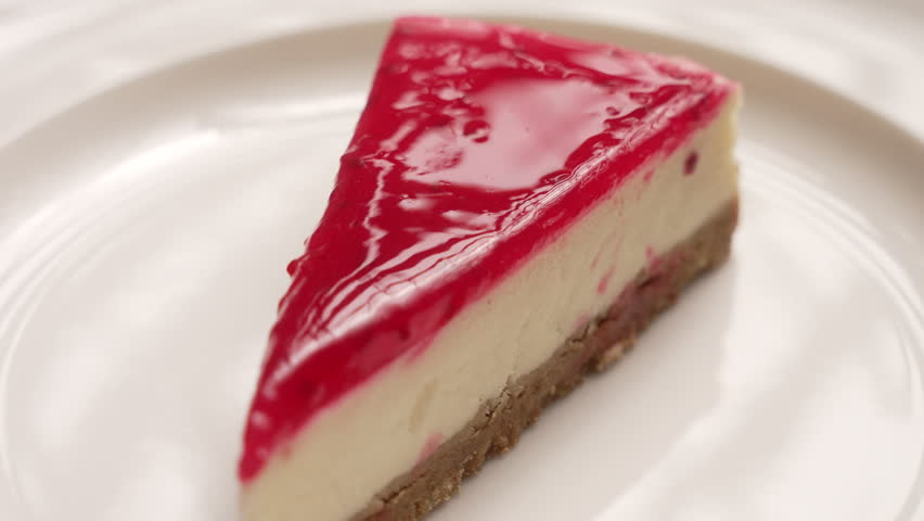 Slice of sweet strawberry cheesecake with red jelly topping rotating on a white plate, fa01