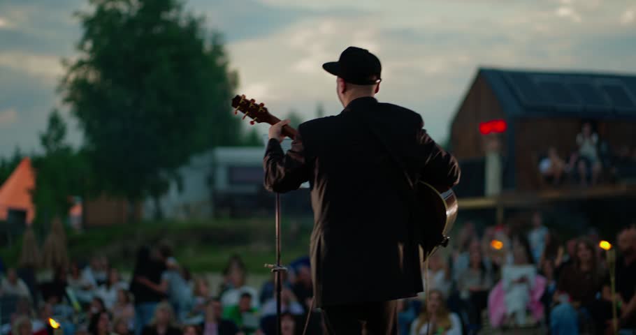 Male acoustic guitarist on outdoor festival stage at sunset
