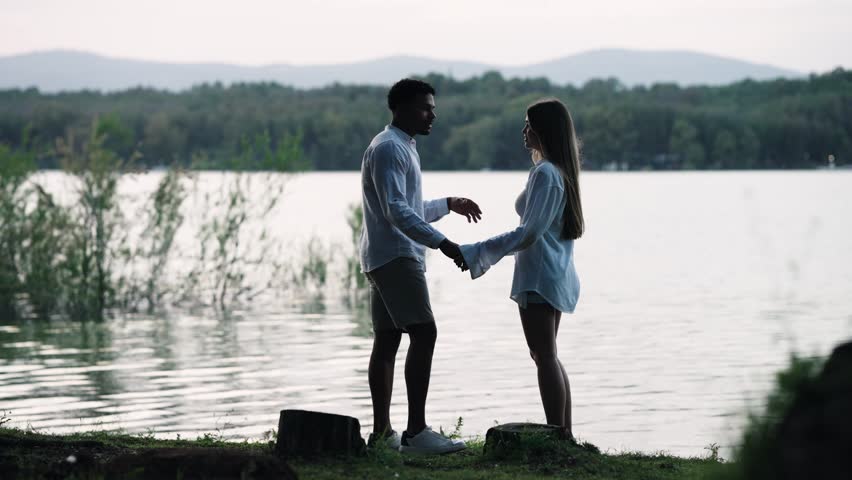 Affectionate diverse couple sharing a tender embrace on the shore of a lake. Romantic scene of a young man and woman in love