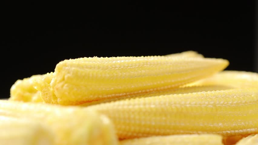 Pile of fresh raw yellow baby corns slowly rotating on black background. Close-up shot