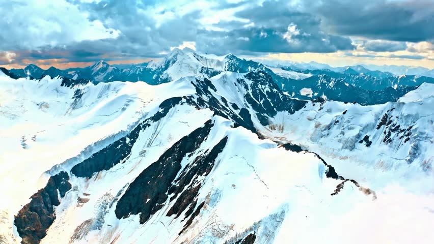 Scenic aerial video showcases a vast expanse of snow-covered peaks and valleys, with clouds drifting across a vibrant sky, capturing the grandeur of a frozen wilderness.