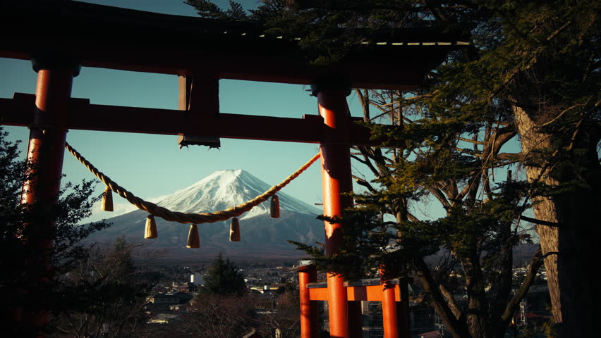 Traditional Japanese torii gate framing snow-capped Mount Fuji above Fujiyoshida beneath a clear blue sky in Japan