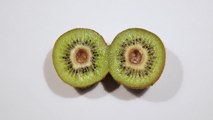 Close-up one fresh kiwi is cut in half on a white background. Rot in the center of the fruit. A spoiled product. Mold inside. Top view. Bad condition. Pareidolia - wide-open surprised eyes. Like face.