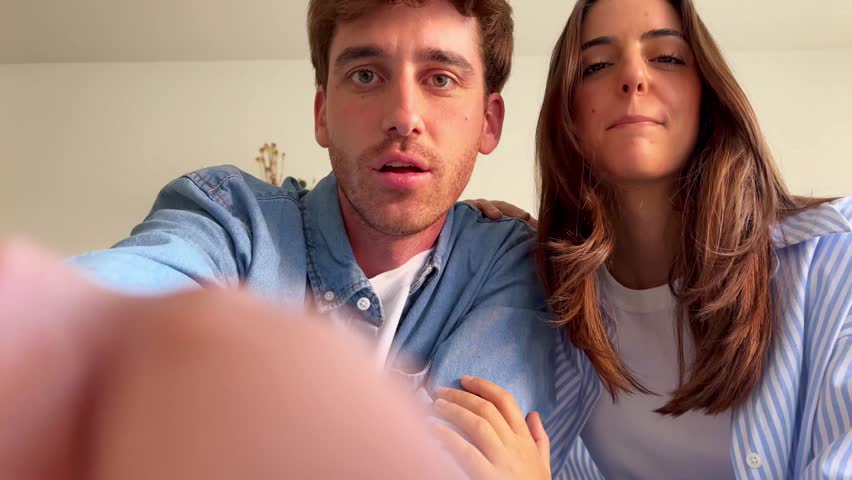 Worried young couple looking down with confused and surprised expressions, trying to understand or fix something out of frame, seen from a low angle point of view inside a home