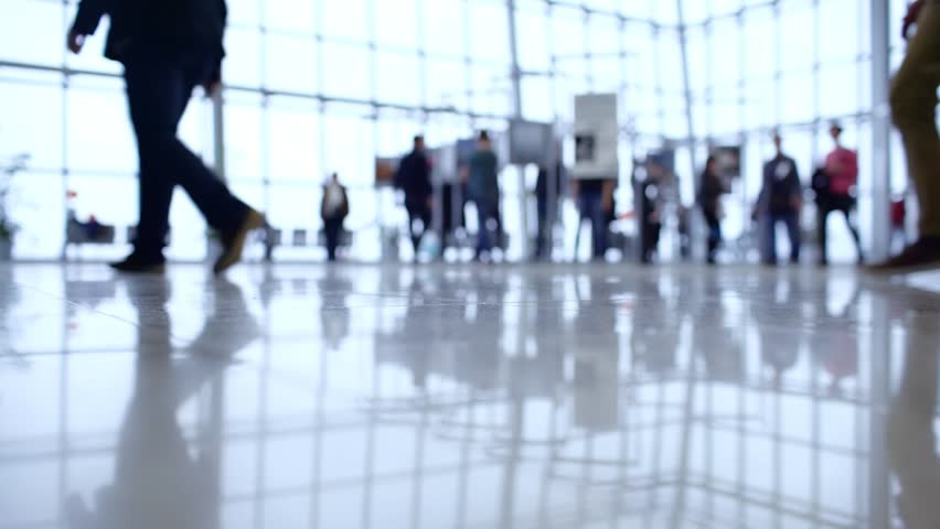 Blurred crowd walks through spacious, bright modern building interior.