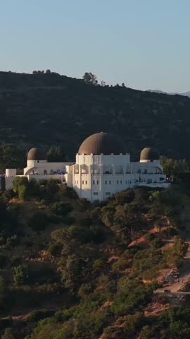 Golden hour light illuminating famous Griffith Observatory in Los Angeles, California surrounded by green Hollywood Hills at sunset, revealing Santa Monica Mountains