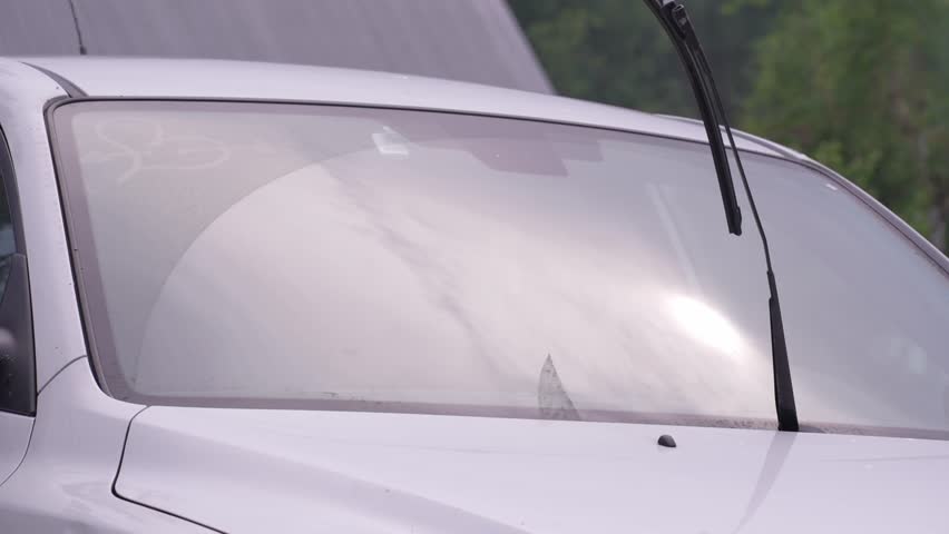 A man washes the car windows with a cloth before applying an anti-rain coating.