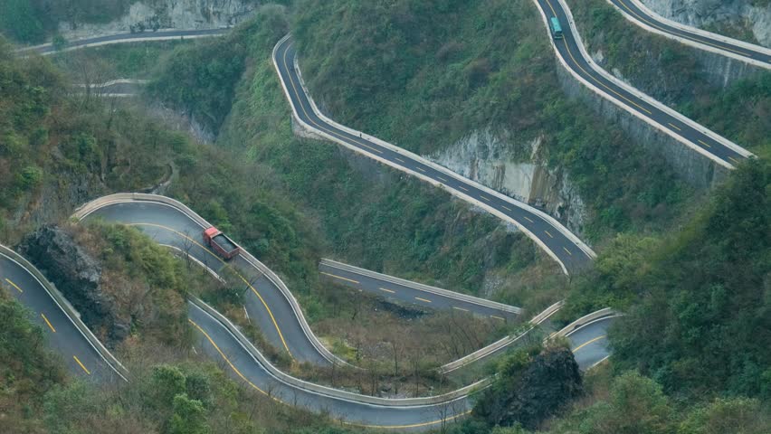 Winding mountain road with sharp hairpin bends carved into steep cliffs in Zhangjiajie, Hunan, China. Travel and tourism landmark. Extreme landscape infrastructure. Vertical orientation