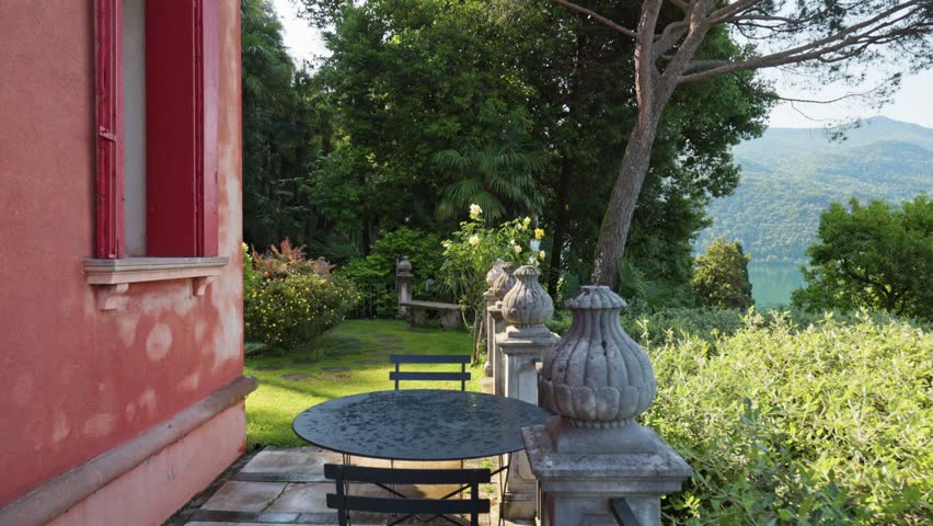 Cozy villa terrace inside Parco Scherrer in Morcote. Beautiful green garden with roses and palms surrounds stone balustrade next to Lake Lugano. Parco Scherrer botanical park, Morcote, Switzerland
