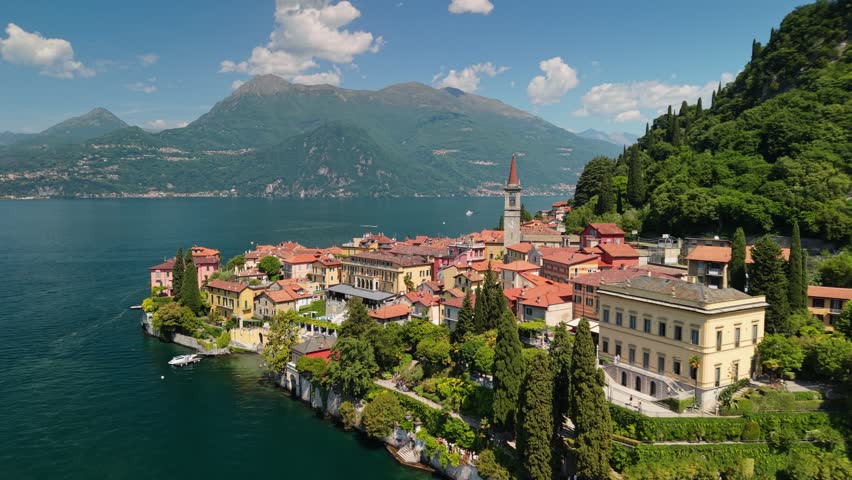 Aerial view of Varenna town with colorful houses on Lake Como. Church tower rises above the historic coastal village in Italy. Shoreline of Lake Como featuring the ancient town of Varenna
