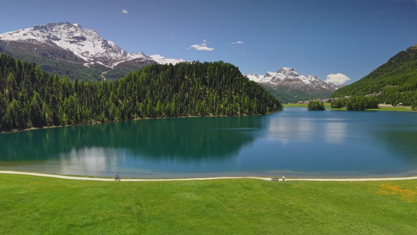 Two cyclists riding along the shore of Lake Champfer, near st Moritz. Aerial shot of people biking on pathway near the emerald water in Switzerland. Alpine nature Lake Champfer