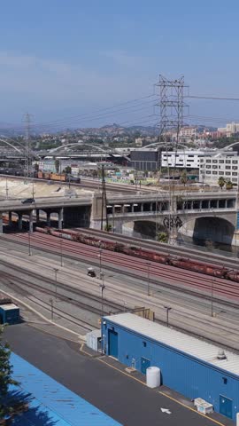 Metrolink passenger train parke in urban Los Angeles rail yard with freight train passing on adjacent tracks and crossing viaduct over LA River