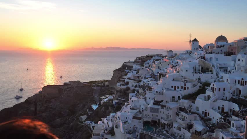 Golden sunset light over whitewashed cliffside houses and sea in Oia, Santorini, Greece.