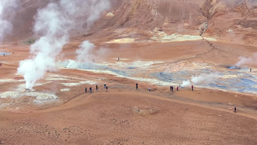 Tourists walking through the barren landscape of the Hverir geothermal area in Iceland, observing hot springs and fumaroles emitting steam