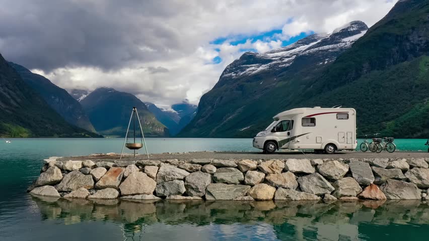 Campervan parked by clear lake in picturesque mountain landscape.