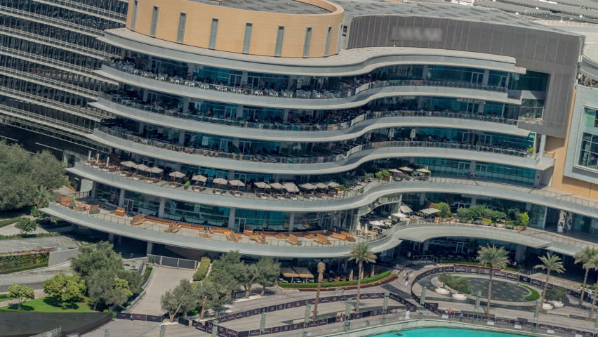 Shopping mall exterior daytime timelapse in Downtown Dubai. Curved shopping mall exterior featuring multi-level outdoor terraces and seating areas. View of the metropolis.