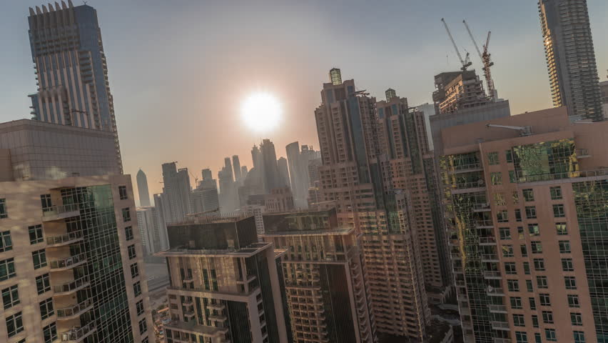 Dense residential high-rises timelapse footage recorded during sunset within Dubai Marina. The setting sun creates a golden haze behind the dense block of skyscrapers. Great planning.