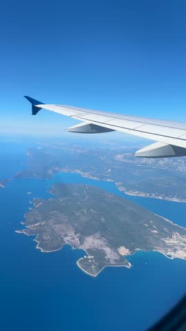 View from airplane window with wing over Montenegro coastline, blue sea, islands and mountains during a sunny flight above the Adriatic coast