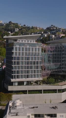 Forwards fly above modern hotel building. Revealing luxury residencies in hills above city. Los Angeles, California, USA