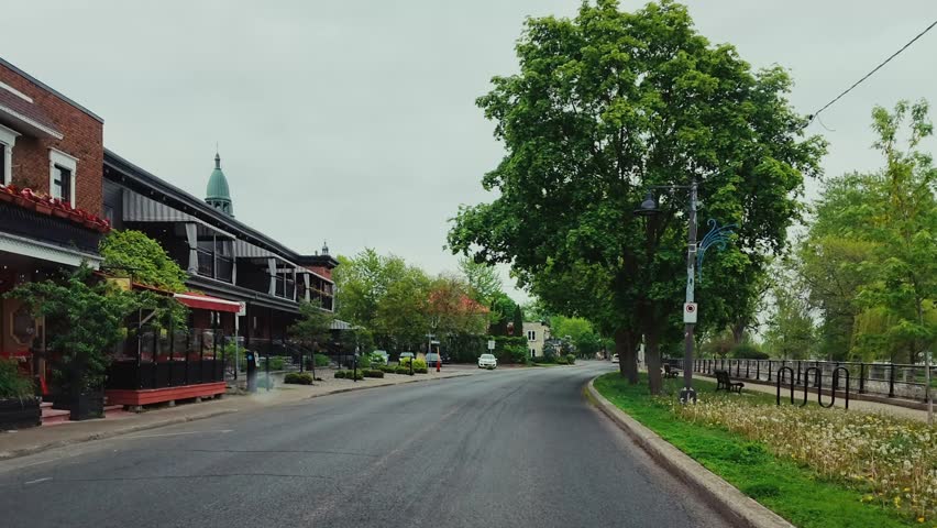 POV driving footage along the Lachine Canal in Montreal, Quebec, Canada. Waterfront pathways, mature trees, and charming neighborhood architecture create a scenic urban landscape along the historic canal.
