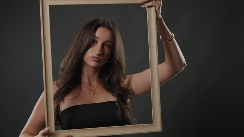 Beauty and self perception concept with a young woman posing in a studio, holding an empty picture frame. This image explores themes of identity, expression, and how individuals frame themselves for t