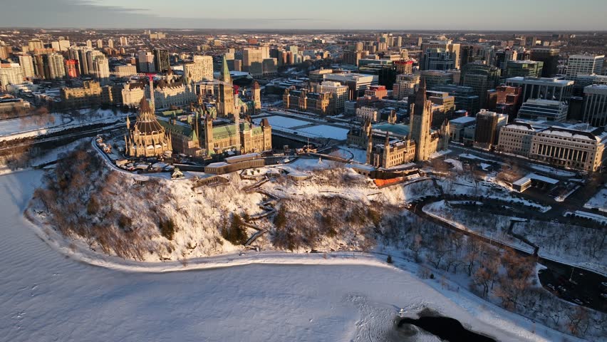 Dynamic drone footage soaring over Parliament Hill Ottawa Canada. Snowy landscape with frozen river and cityscape. Historic architecture.