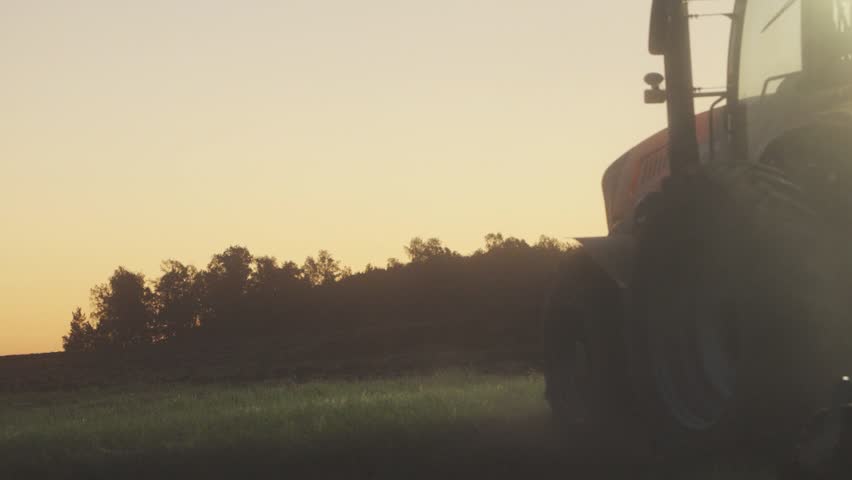 Farm Tractor Working Through Dust At Sunset With Sun Rays And Warm Golden Light Across Agricultural Field